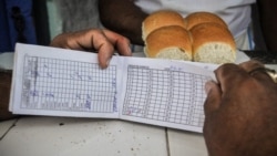 Una cubana muestra su vieja libreta de racionamiento junto a una ración de pan. (AFP/Archivo)