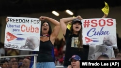 Asistentes al partido entre EEUU y Cuba levantan carteles con mensajes de protesta contra el régimen cubano. (AP/Wilfredo Lee)