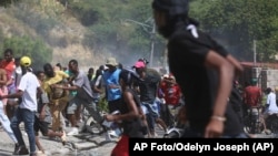 Un grupo de personas huye del gas lacrimógeno disparado por la policía para dispersar a los manifestantes que exigen a la policía y al primer ministro que actúen de inmediato contra las pandillas, en Puerto Príncipe, Haití, el lunes 19 de agosto de 2024. (AP Foto/Odelyn Joseph)