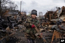 Yehor, de 7 años, de pie con un rifle de madera junto a vehículos militares rusos destruidos cerca de Cherníhiv, Ucrania, el domingo 17 de abril. (AP/Evgeniy Maloletka)