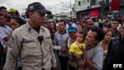 Un hombre con un niño en brazos grita consignas a un policía durante una protesta para exigir alimentos en el sector popular Catia, en Caracas (Venezuela).