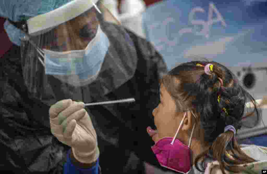 Una empleada de salud toma una muestra para una prueba de COVID-19 a una niña que acaba de llegar desde Cancún, México, en el Aeropuerto Internacional José Martí de La Habana, el domingo 15 de noviembre de 2020. (AP Foto/Ramon Espinosa)