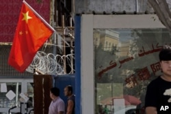 Residentes esperan cerca de las alambradas y una bandera nacional china en una comunidad de Peyzawat, en la región china de Xinjiang.