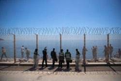 Guardas marroquíes vigilan una valla fronteriza que divide al país con España mientras algunos migrantes caminan en la zona, en Ceuta, el 19 de mayo de 2021. (AP Foto/Mosa'ab Elshamy)