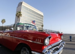 Un auto clásico pasa con una bandera de Estados Unidos frente a la embajada de ese país en La Habana.