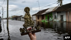 Una mujer alza una imagen de la Virgen de la Caridad del Cobre en las calles inundadas deBatabano, en Mayabeque, en septiembre pasado. (Yamil Lage/AFP)