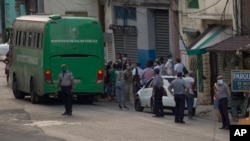 Sospechosos de coronavirus son evacuados en un bus del MINSAP y escoltados por la policía cerca del Mercado de Cuatro Caminos, en La Habana. (AP/Ismael Francisco)