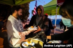 Un migrante, centro, recibe una comida caliente de parte de voluntarios afuera de la Iglesia del Sagrado Corazón en el centro de El Paso, Texas, el sábado 7 de enero de 2023. (AP/Andres Leighton)