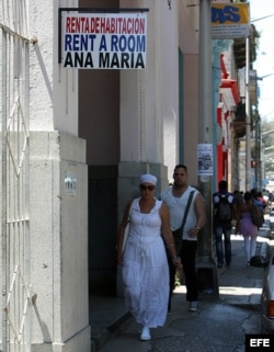 Varias personas pasan junto a un cartel de renta de habitaciones en La Habana