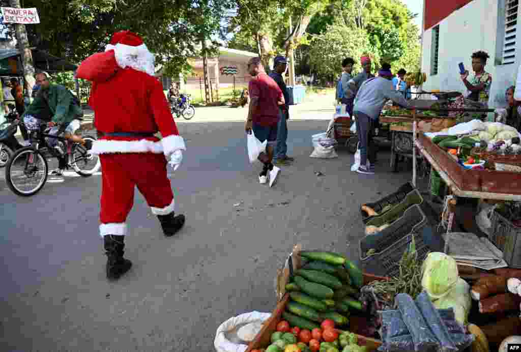 Santa Claus pasa delante de un puesto de viandas, en La Habana.