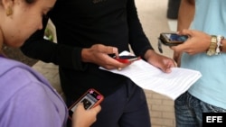 Tres jóvenes usan sus teléfonos móviles en La Habana, Cuba.