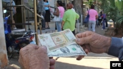 Un hombre muestra un peso convertible cubano y un dólar estadounidense frente a una oficina de la Western Union en La Habana.