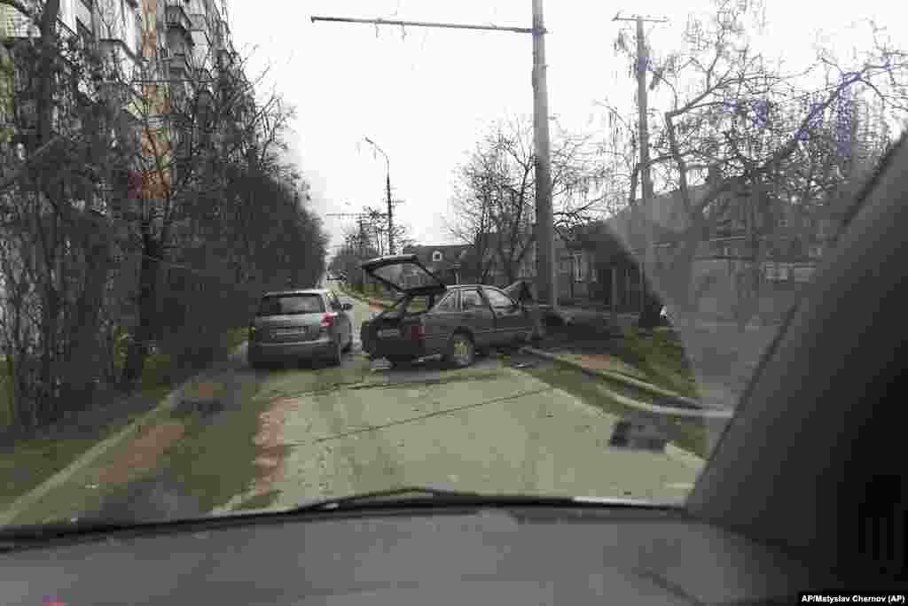 Un carro trata de escapar del bombardeo ruso pasando al lado de un carro que choco contra una cerca en Mariúpol, Ucrania. Foto: AP/Mstyslav Chernov.