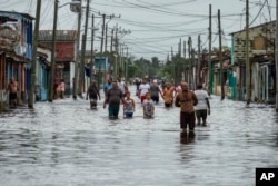 Varias personas caminan por una calle inundada tras el paso del huracán Helene, en Batabanó, provincia de Mayabeque, Cuba, el jueves 26 de septiembre de 2024. (Foto AP/Ramon Espinosa)