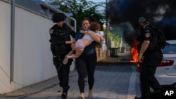 Agentes de policía israelíes evacuan a una mujer y un niño de un lugar alcanzado por un cohete disparado desde la Franja de Gaza, en Ashkelon, sur de Israel, el 7 de octubre de 2023. AP Photo/Tsafrir Abayov.