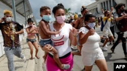 Una mujer con un niño en brazos marcha frente al Capitolio de La Habana durante una manifestación contra Miguel Díaz-Canel en La Habana, el 11 de julio de 2021. (Adalberto Roque/AFP).