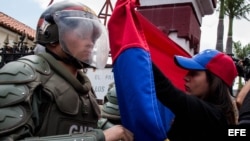 Una mujer sostiene una bandera de Venezuela frente a integrantes de la Guardia Nacional Bolivariana.