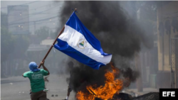 Un joven corre con la bandera de Nicaragua frente a unas llantas incendiadas ayer en la ciudad de Masaya (Nicaragua). EFE