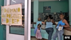 Una mujer hace cola en una farmacia de La Habana junto a un cartel alusivo al Primero de Mayo.