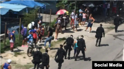 Boinas negras caminan junto a personas que permanecen en una cola.